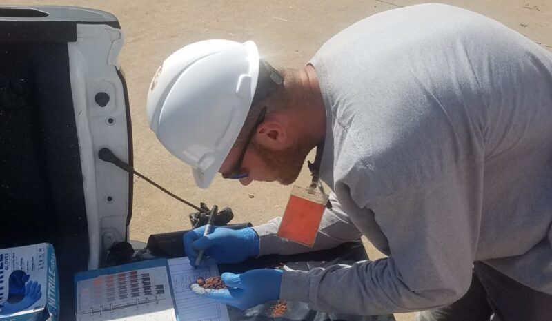 20190725_104634 person looking at dirt and writing in book on the back of a truck bed