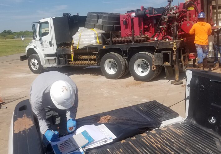 person looking at dirt while writing and equipment in background
