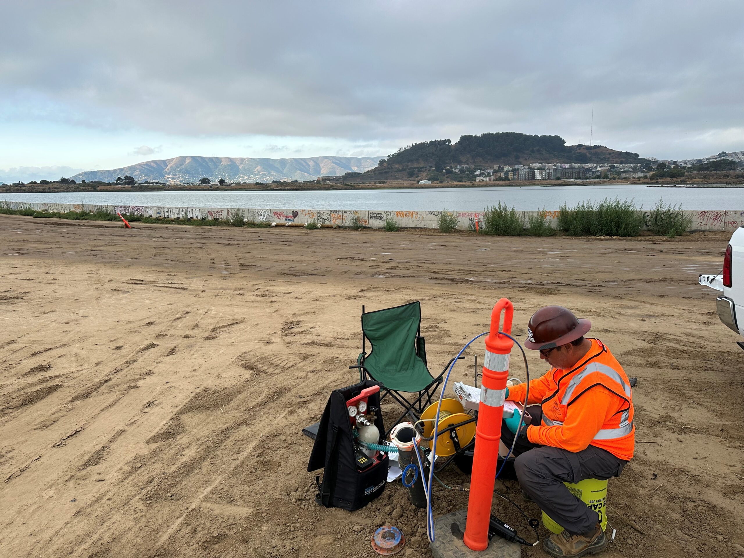 person working with equipment in sandy area near water and mountains in horizon