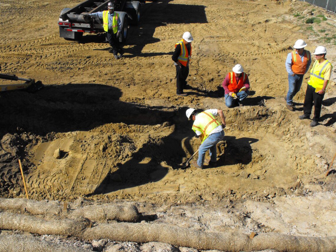 construction workers watching one man dig in dirt