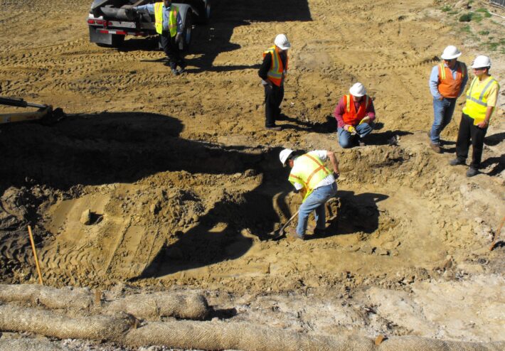 construction workers watching one man dig in dirt