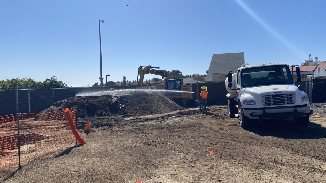 water truck and person spraying large dirt pile