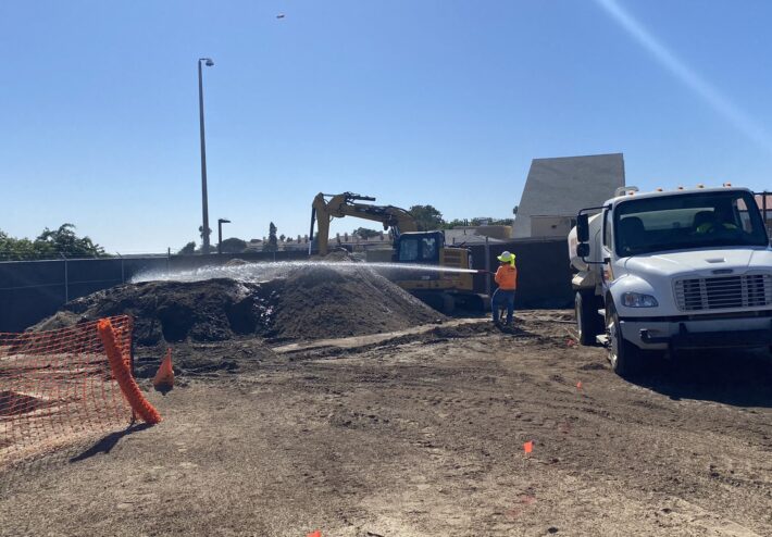 water truck and person spraying large dirt pile