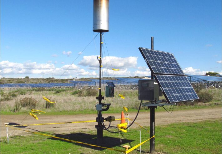 small solar panel and tall equipment with large solar field behind