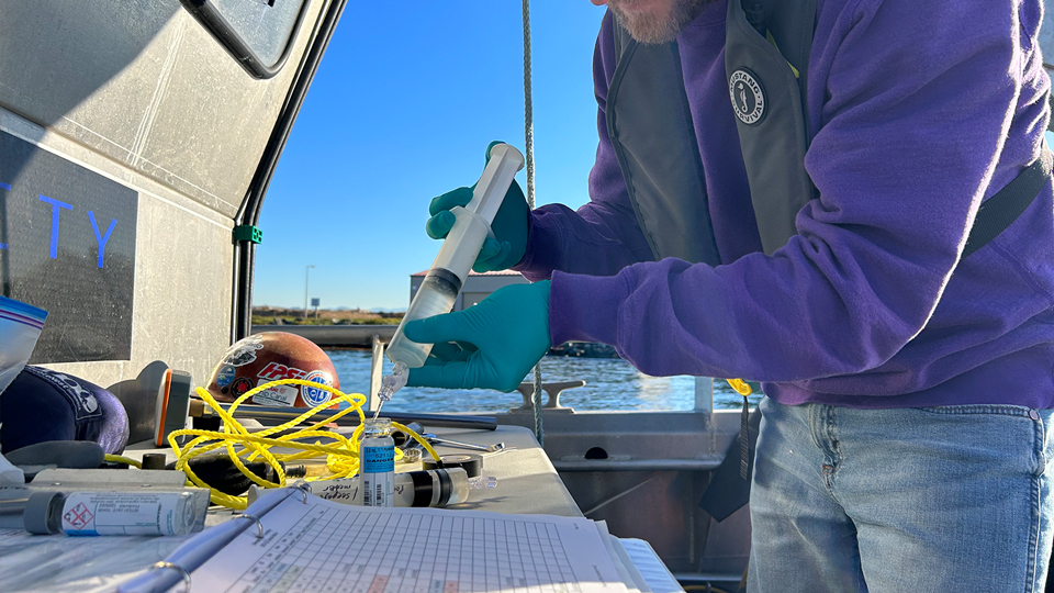 person sampling water with large syringe into vials and equipment