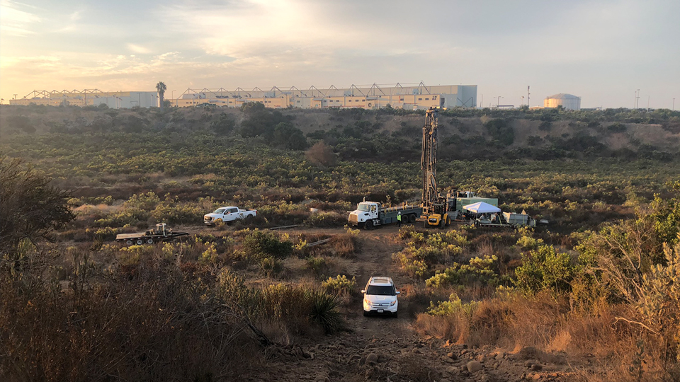 white trucks in brush field with large building on the horizon